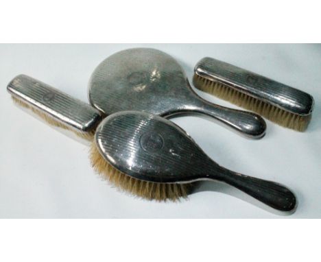 Three Edwardian silver-mounted brushes and a hand mirror, engine-turned, Birmingham 1907.