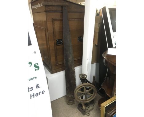 A vintage cast iron bench drill and a two handled logging saw.