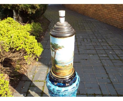 A large table lamp base the cylindrical stem hand painted with a landscape mounted on a ceramic black base with gilded accent