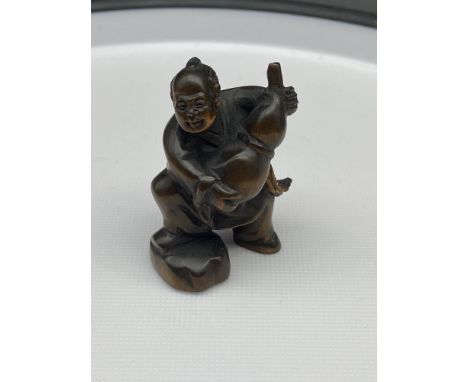 A Japanese hand carved netsuke of a gentleman carrying a flagon of wine. Signed. 