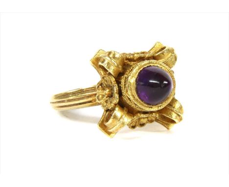 A gold amethyst ring, with a cabochon amethyst, rub set to a square head with applied twisted wire, scroll and floral decorat