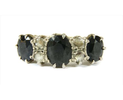 An 18ct gold sapphire and diamond ring, with a graduated row of three oval mixed cut sapphires, with pairs of rose cut diamon