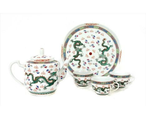 A Chinese tea service, comprising a teapot and cover, three teacups and a circular tray, all painted with dragons amongst clo
