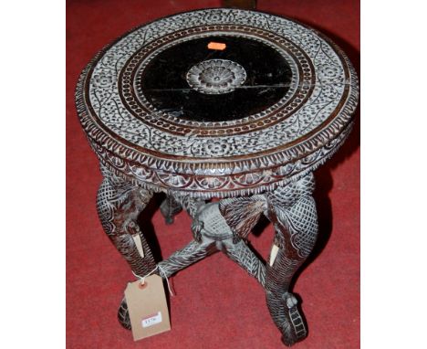 An Indian ebonised hardwood low relief carved circular occasional table, raised on elephant trunk supports