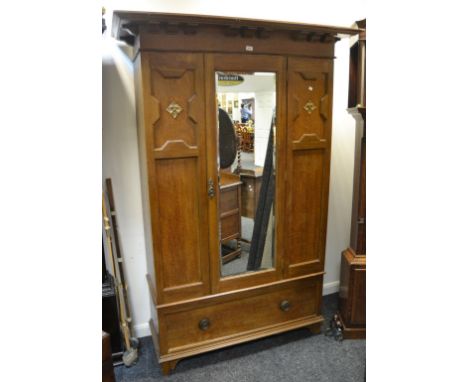 An early 20th century oak wardrobe, large oversailing cornice above central mirrored door, flanked by panelled doors, plinth 