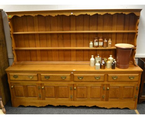 A 20th century light oak substantial dresser, ogee cornice, shaped supports holding two plate racks, out stepped face enclosi