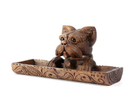 A BLACKFOREST LINDEN WOOD DOG INKWELL AND PEN TRAY LATE 19TH / EARLY 20TH CENTURY with glass eyes, the head hinged to reveal 
