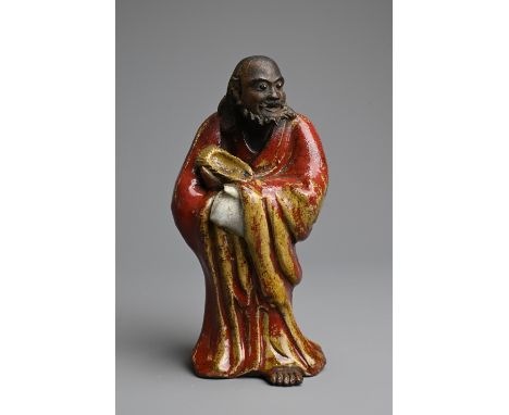 A CHINESE GLAZED SHIWAN POTTERY MODEL OF DAMO, 19/20TH CENTURY. Standing bare foot dressed in robe, covered in a reddish brow