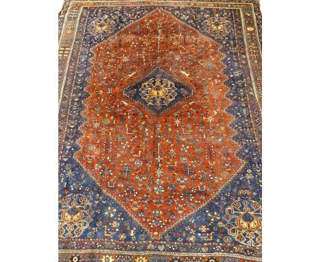 A Shiraz carpet, with a design of geometric motifs on a red ground with navy spandrels, multiple borders, 300cm x 230cm.