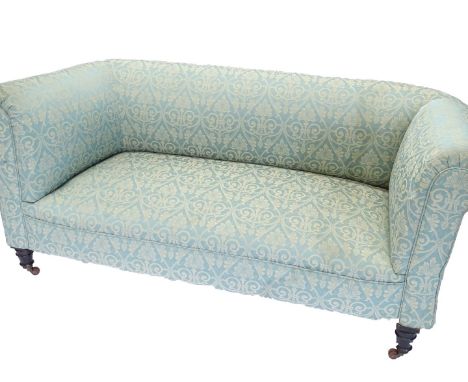 A Victorian ebonised drop arm Chesterfield sofa, upholstered in blue and gold fabric on turned tapering legs with ceramic cas