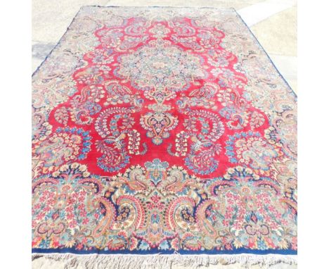 A large Kirman carpet, with a central medallion, on a red ground, with floral borders and spandrels, 459cm x 319cm.
