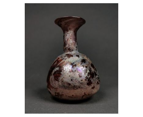 Ca.100 AD. A finely modeled Ancient Roman translucent aubergine glass unguentarium of a large size, featuring a flat base, gl