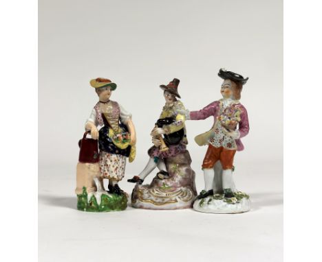 A Meissen style figure of a Harlequin, his costume decorated with playing cards, playing a bagpipe, on a Rococo scroll base, 