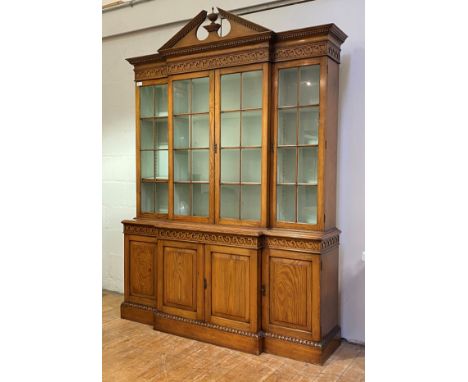 A pitch pine breakfront bookcase in the Georgian taste, second half of the 20th century, the dentil cornice with urn finial a