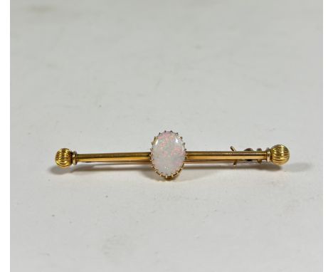 An opal-set yellow metal bar brooch, the oval-cut opal on a cylindrical bar with reeded ball terminals, unmarked. Length 58mm