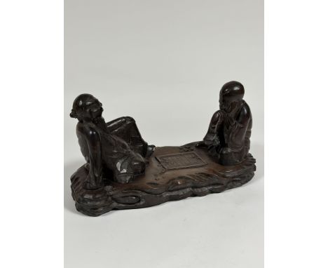 A Chinese carved wooden group of two seated figures playing "Go", unsigned. Height 23cm, length 43cm