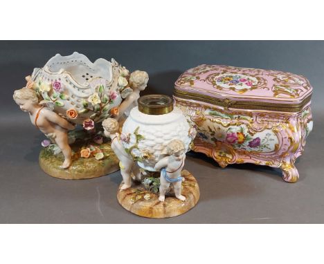 A German porcelain lamp base in the form of a basket held by three Putti together with a similar bowl and a similar casket 