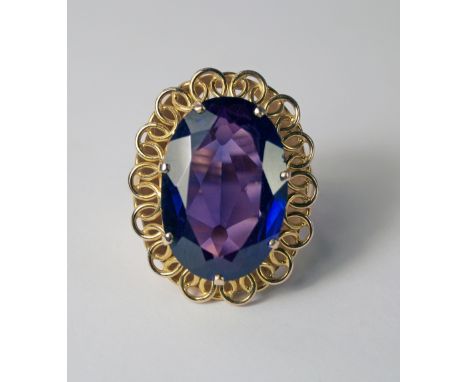 A synthetic Alexandrite dress ring, the oval cut stone set in high ct yellow metal, an entwined circle border leading to spli