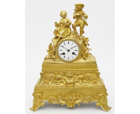 Figürliche Pendule. Feuervergoldete Bronze. Hoher, reich reliefierter Sockel auf vier Füßen. Uhrengehäuse in Form eines Felse