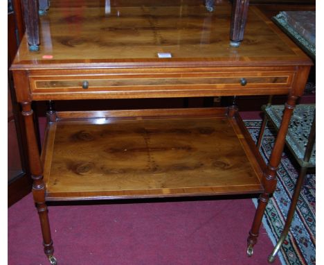 A reproduction yew wood two-tier side table, having single frieze drawer raised on brass roller castors, width 77cm