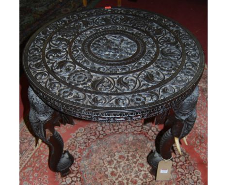 A circa 1900 Indian heavily carved hardwood circular occasional table, raised on elephant trunk supports with ivory tusks (on