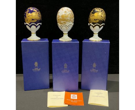 A set of three Royal Crown Derby Fabergé eggs, with stands, Gold Aves pattern, Black Aves pattern and Gold Aves pattern on Co
