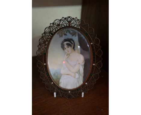 E.W., a three quarter length portrait of a lady in a landscape, initialled, on ivory, 13.7 x 9.7cm oval, in a filigree frame.