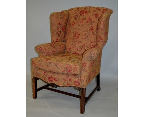 A GEORGE III DESIGN MAHOGANY FRAMED WING ARMCHAIR, shell carved frieze, moulded square legs united by a “H” shape stretcher, 