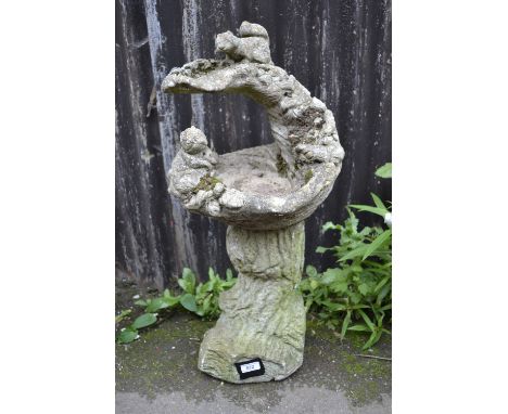 A reconstituted stone bird bath, squirrels on a trunk