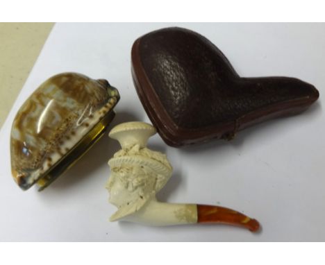 A miniature antique carved pipe of a figure head, cased, length of case 8cm together with a 19th Century Cowrie Shell snuff b