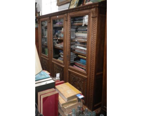 A large Continental carved light oak bookcase fitted three glazed doors with carved panels below resting on paw feet, 76" hig