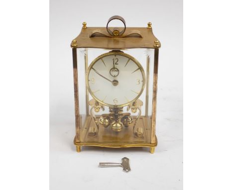 A vintage Kundo mantle clock with brass and glass casing surround, scrolled handle, open movement and in with key.