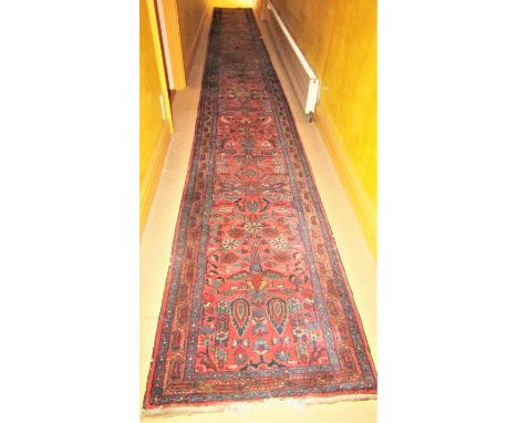 A very long eastern wool runner with repeating floral detail upon a salmon pink ground within narrow alternating borders, 750