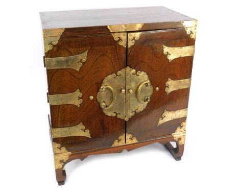 An early 20thC Korean elm and brass bound table cabinet, the two doors opening to reveal a shelf above a pair of small frieze