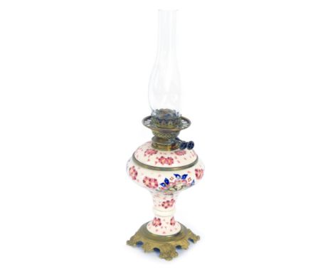 A 20thC ceramic oil lamp, on a white ground with pink flowers, on embossed brass base, with chimney, 59cm high. 