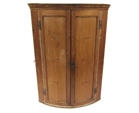 A Georgian pine corner cupboard, with a banded top above two curved doors, with a fitted two shelf interior, 137cm high, 98cm