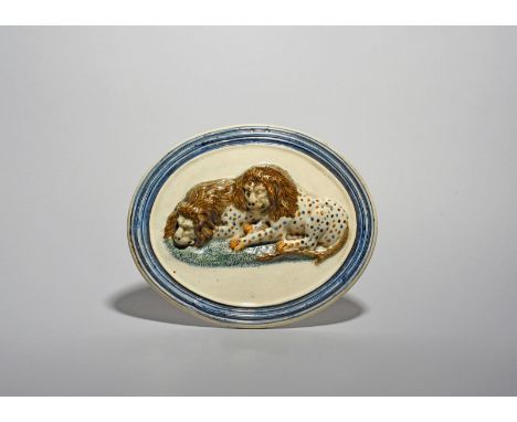 A good Prattware plaque, c.1800, moulded in high relief with two recumbent lions, their coats decorated with dots in blue, ma