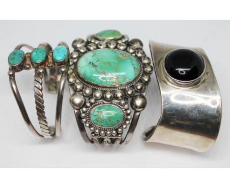 A group of three white metal bangles comprising two set with turquoise cabochons and another of Modernist form set with a bla
