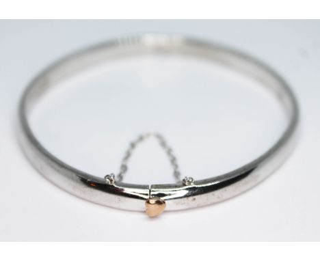 A Clogau Welsh silver bangle with gold heart push button release clasp button, diam. 56mm, wt. 19.19g, with box.  Condition -