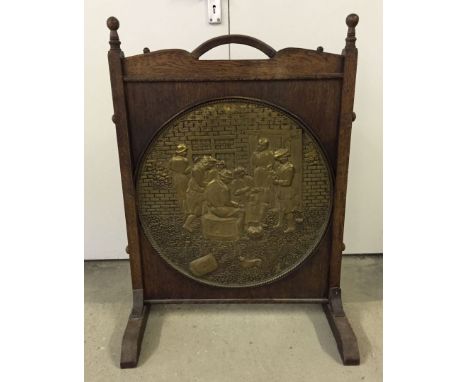 A large vintage wooden firescreen with central brass roundel depicting a tavern scene. Screen measures 63cm wide and 88cm tal