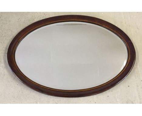 An oval mirror with inlaid wood surround. Approx 77cm wide.