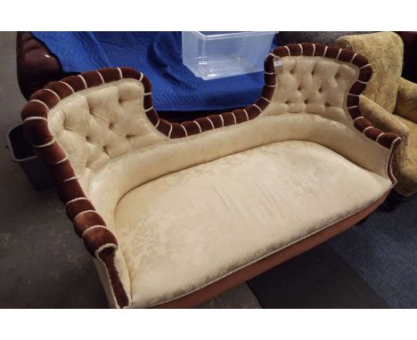 A double ended Edwardian sofa with arched backs in cream and brown upholstery resting on tapering supports