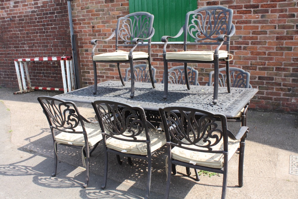 A LARGE CAST METAL GARDEN TABLE AND 8 CHAIRS WITH CUSHIONS