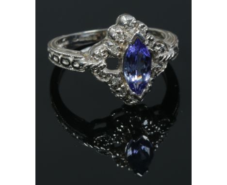 A 14ct white gold ring set with a marquis cut tanzanite stone and diamonds and with milgrain borders. Size O.