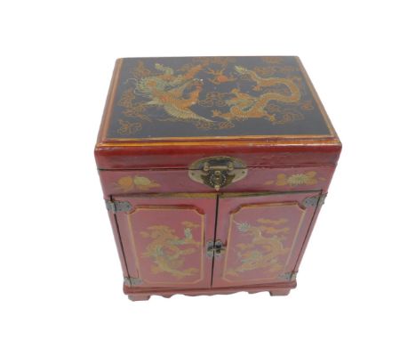 A 20thC Chinese red lacquer table cabinet, decorated with figures at a table, dragons and birds, the lid opening to reveal a 