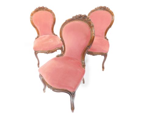 A set of three Victorian walnut balloon back salon chairs, with a rose carved crest rail, red draylon overstuffed seat and bu