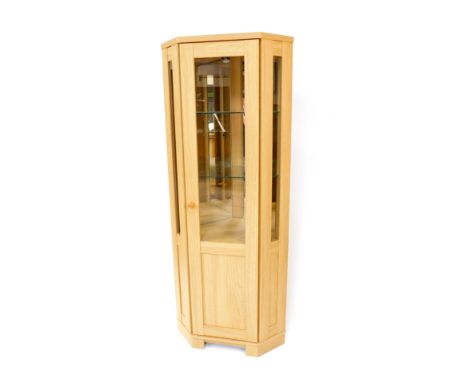 A light oak corner display cabinet, with half glazed door and side panels, opening to reveal two glass shelves, with cupboard