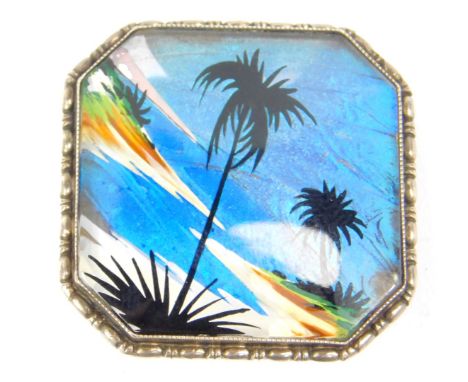 A vintage 1920's butterfly wing brooch, of canted square form, the central panel decorated with palm trees over the shores of