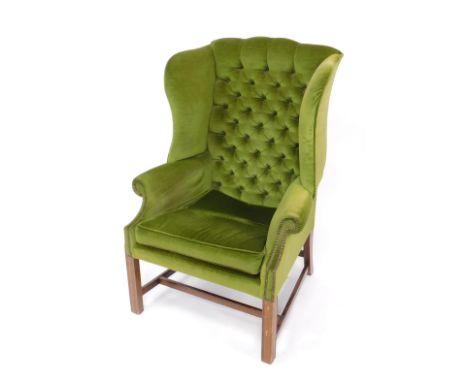 A George III style mahogany wingback armchair, upholstered in button back green draylon, raised on fluted square legs, united