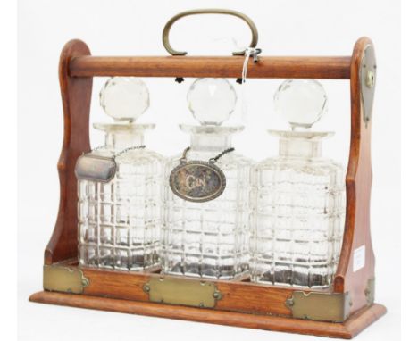 An Edwardian oak three bottle tantalus, with a silver whisky bottle ticket